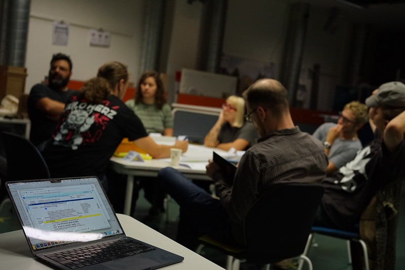 People discussing around a table in the background, focus is given on the laptop which shows the timetable for the workshop.